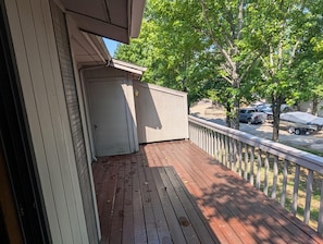 Eine Holzterrasse mit einer weißen Tür, einem weißen Zaun und Blick auf geparkte Autos und Bäume.
