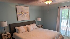 Ein Schlafzimmer mit einem großen Bett, zwei Nachttischen, einem Deckenventilator und einem Fenster mit Vorhängen.