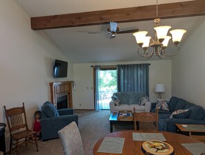 A living room with a fireplace, a ceiling fan, a chandelier, and a television mounted on the wall. - ON THE ISLAND (Holiday Island)