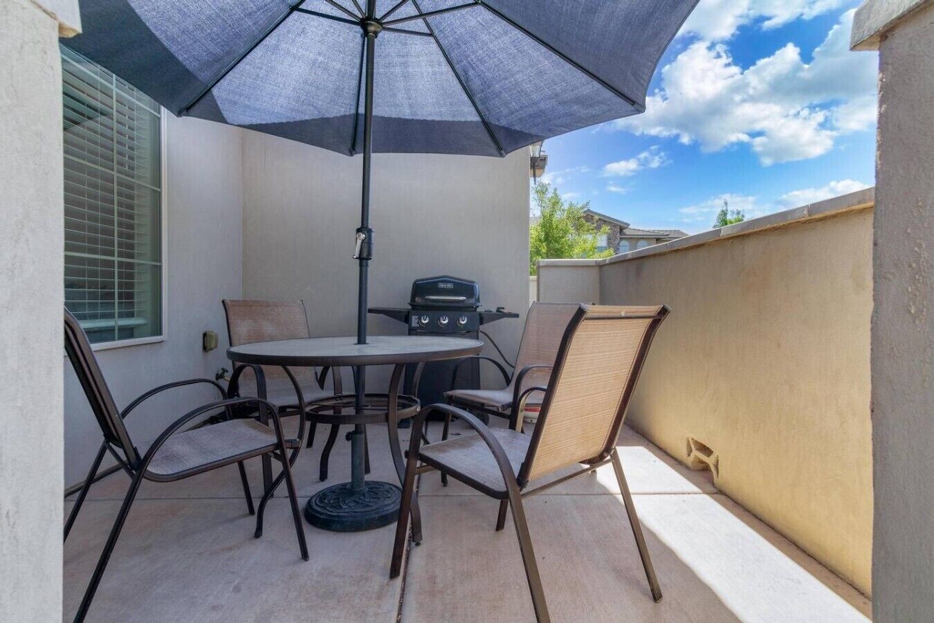 A patio with a round table, four chairs, a grill, and a large umbrella.