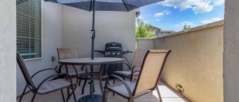 A patio with a round table, four chairs, a grill, and a large umbrella.