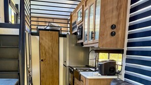 A compact kitchenette with a refrigerator, microwave, and stove, a wooden cabinet, and a leather couch.