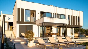 Ein modernes, zweistöckiges Haus mit Balkon, Pool und Liegestühlen.