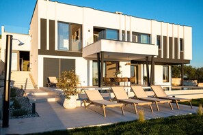 Una casa moderna de dos pisos con balcón, piscina y sillas de descanso.