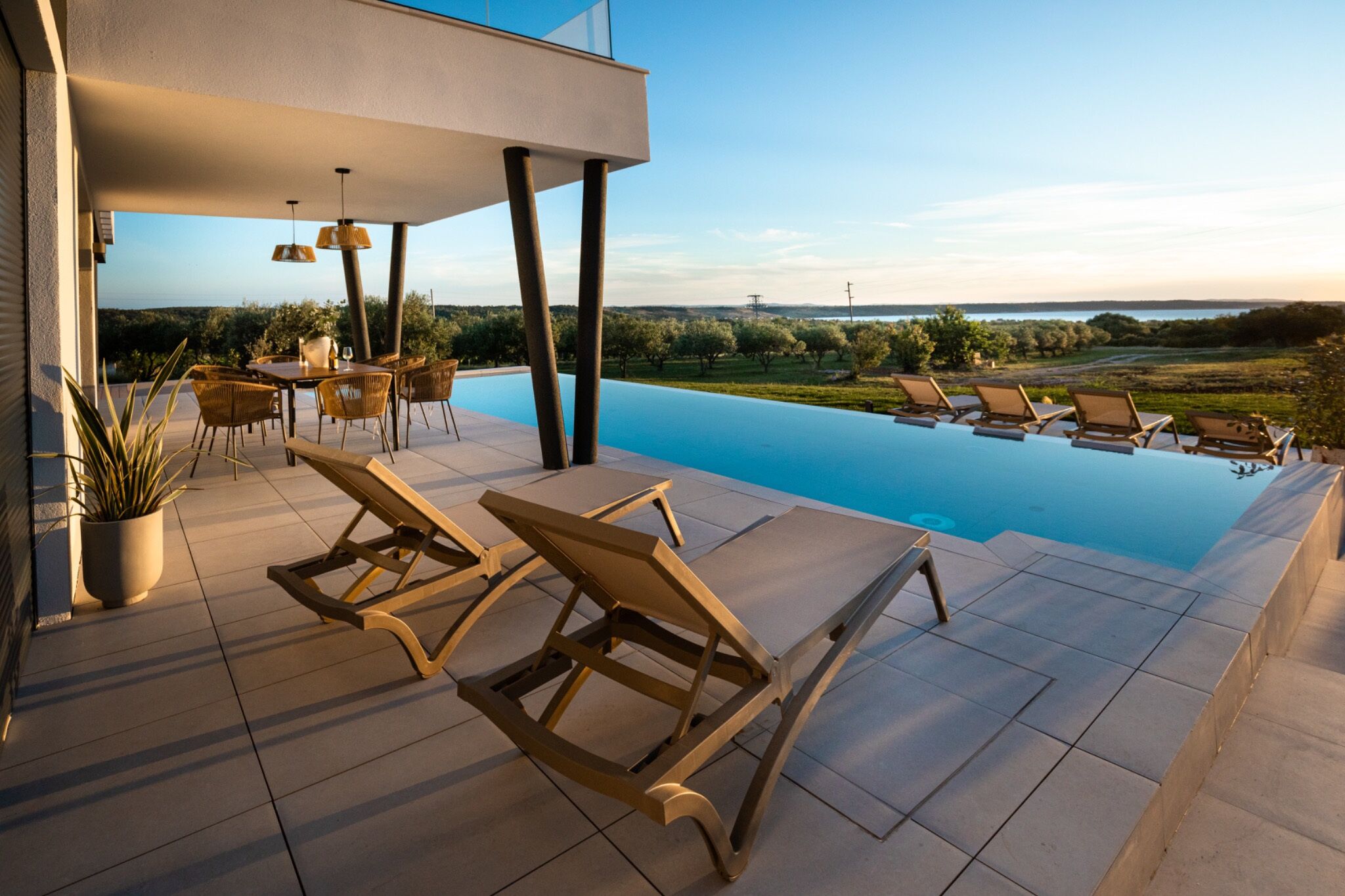 A modern outdoor pool area with lounge chairs, a table, and a view of the landscape.