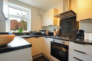 A modern kitchen with white cabinets, a black countertop, a microwave, a stove, and a window with a view of a brick building. - Chesterfield 2 Bed, near town, hospital and Peaks (Calow)