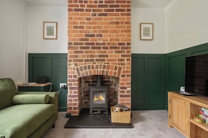 A living room with a brick fireplace, green walls, a green sofa, and a wooden cabinet. - Chesterfield 2 Bed, near town, hospital and Peaks (Calow)