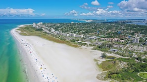 Eine Luftaufnahme einer Küstenstadt mit einem breiten Sandstrand, einem Jachthafen und dichter städtischer Bebauung.