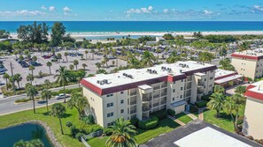 Ein mehrstöckiges Hotel mit rotem Dach, umgeben von einem Parkplatz und Palmen, mit Blick auf einen Strand.
