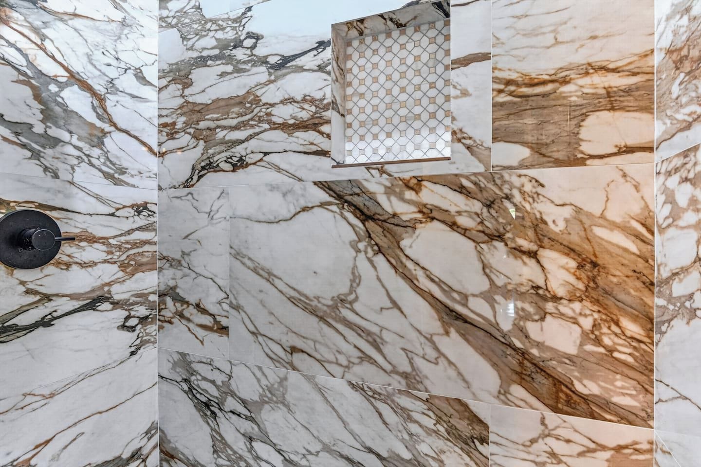 A wall with a marble pattern, a black faucet, and a small window with a geometric pattern.