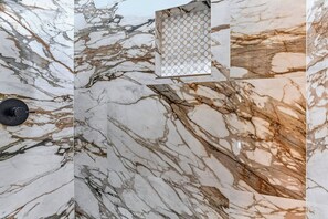 Pared con diseño de mármol, un grifo negro y una ventana pequeña con un patrón geométrico.