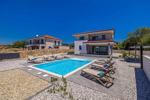 A pool area with lounge chairs, a swimming pool, and two buildings with balconies. - Villa ADRIA MOMENTS with private pool (Pinezići)