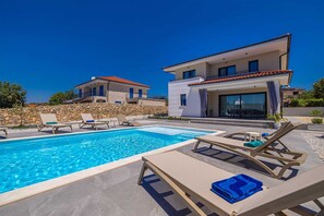 A modern two-story house with a swimming pool, stone walls, and outdoor furniture.