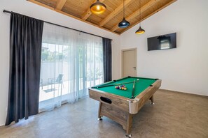 A pool table in a room with a wooden ceiling, large windows with curtains, and a door. - Villa ADRIA MOMENTS with private pool (Pinezići)