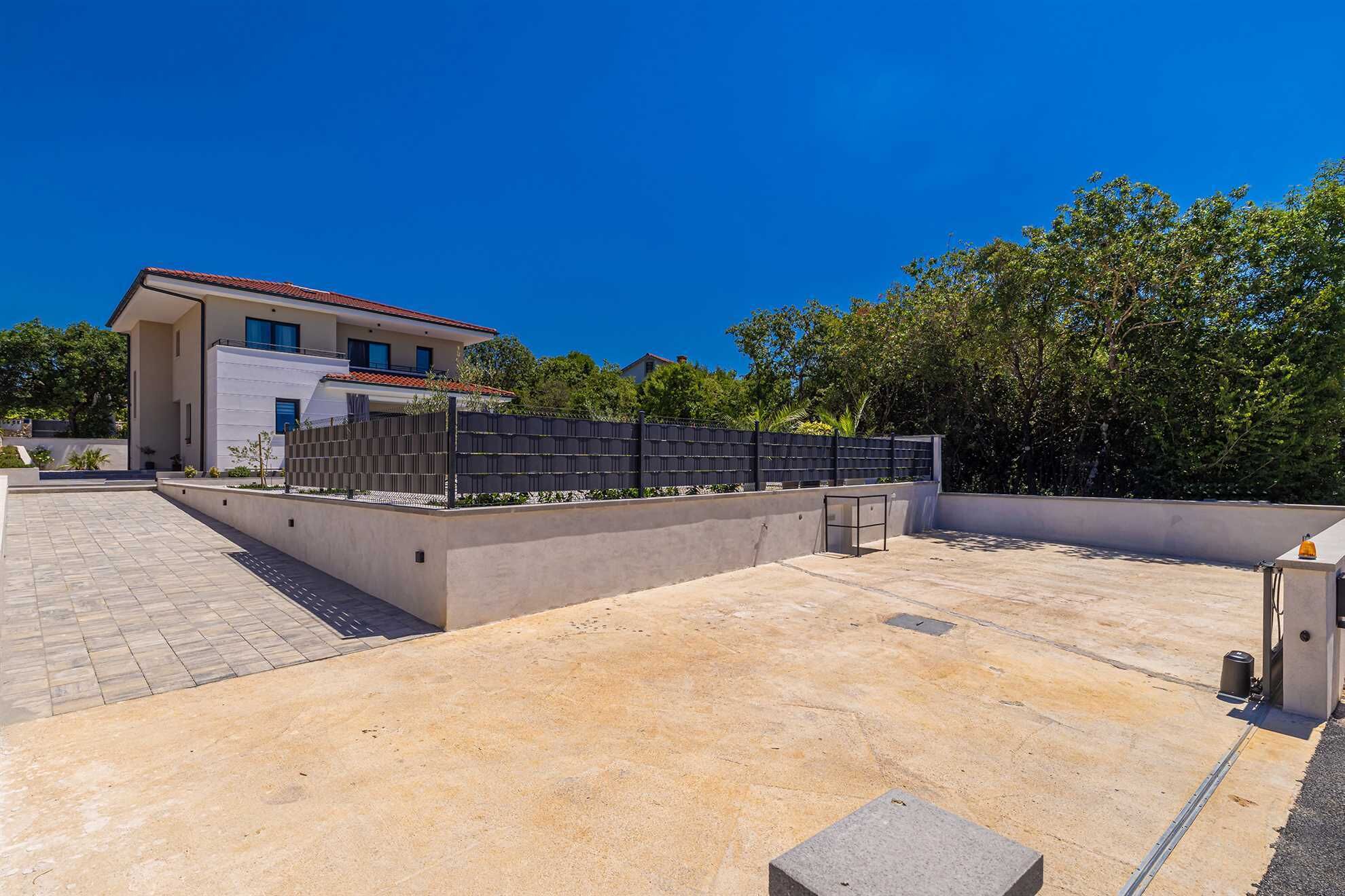 A modern building with a flat roof, a paved patio area, and a black fence.
