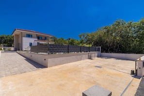 A modern building with a flat roof, a paved patio area, and a black fence. - Villa ADRIA MOMENTS with private pool (Pinezići)