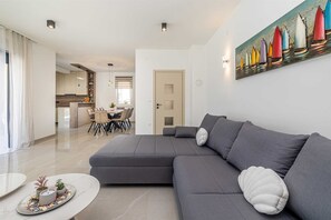 A modern living room with a sectional sofa, a dining area, and a kitchen in the background.