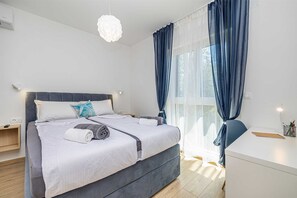 Ein modernes Schlafzimmer mit Bett, Nachttischen, Schreibtisch und einem Fenster mit Vorhängen.