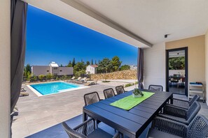 Ein Poolbereich mit Tisch und Stühlen, einem Schwimmbecken und Blick auf Gebäude und Bäume.