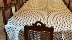 Un lungo tavolo da pranzo con una tovaglia fantasia, circondato da sedie di legno con schienali intrecciati.