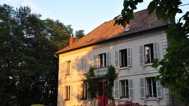 Un edificio a due piani con una porta rossa, diverse finestre con persiane e un balcone.