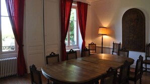 Una sala da pranzo con un grande tavolo di legno, tende rosse, una lampada da terra e un'ampia opera d'arte incorniciata appesa al muro.