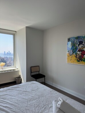 A hotel room with a large window, a bed, a chair, and a wall-mounted painting. - Million dollar view 2-bedroom apartment in New York with AC and gym access (New York)