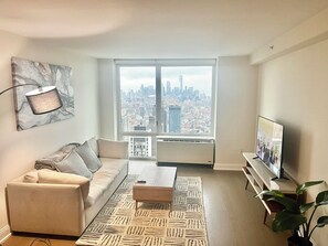 Ein modernes Wohnzimmer mit Blick auf die Stadt, ausgestattet mit einer Couch, einem Couchtisch, einem Fernseher und einer Pflanze.