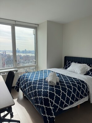 Ein Hotelzimmer mit großem Fenster, einem Bett mit gemustertem Überwurf, einem Schreibtisch und einem Sessel.