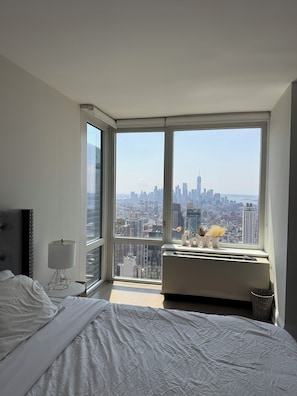 Ein Schlafzimmer mit großem Fenster, einem Bett, einer Nachttischlampe und einem kleinen Tisch mit Dekoration.