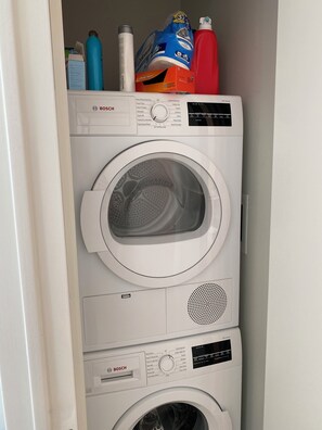Un lave-linge à chargement frontal de la série 300 de Bosch, doté d’un panneau de commande et d’une étagère supérieure où sont rangées différentes lessives.