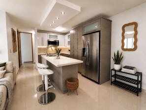 A modern kitchen with a central island, stainless steel appliances, and a minimalist design. - AÜRA - Beachfront Sųites + Pool @ Isla Verde (Carolina)