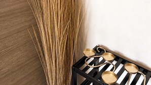 Ein Zimmer mit einer holzig strukturierten Wand, einer hohen Zierpflanze, einem Spiegel mit gewelltem Rahmen und einer schwarz-weißen gestreiften Ablage mit Schalen.