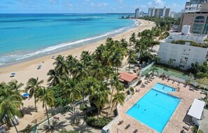 A beachside hotel with a swimming pool, palm trees, and a view of the ocean. - AÜRA - Beachfront Sųites + Pool @ Isla Verde (Carolina)