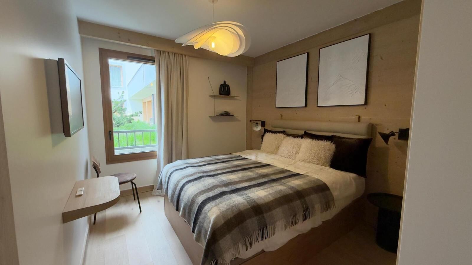 Une chambre à coucher comprenant un lit, un bureau, une chaise, une fenêtre avec des rideaux et deux tableaux encadrés accrochés au mur.