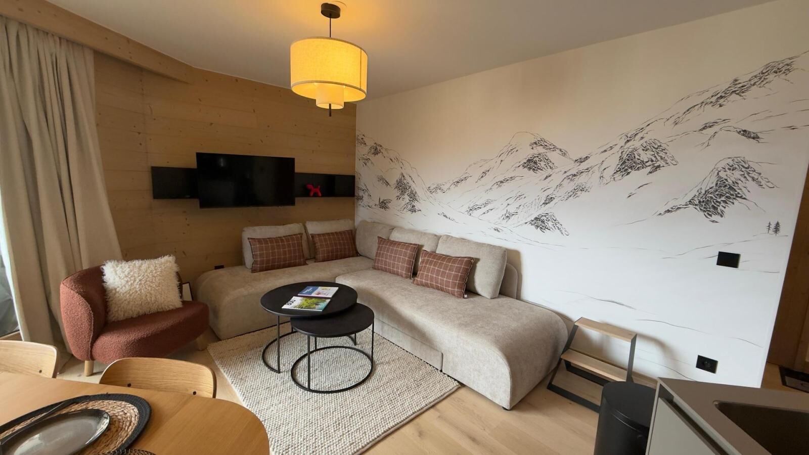 Ein modernes Wohnzimmer mit einer Couch, einem Couchtisch, einem Fernseher und einer Wand mit einer Bergmalerei.