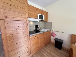 A compact kitchen with wooden cabinets, a microwave, a sink, and a small trash bin. - 50m from ski slopes, 2nd floor, swimming pool, balcony, ski locker, 32m², Vars (Vars)