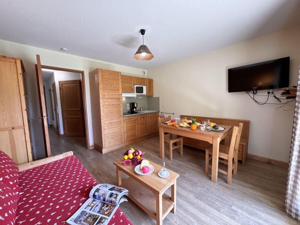 A compact room with a bed, a dining table with chairs, a kitchen area, and a TV mounted on the wall.