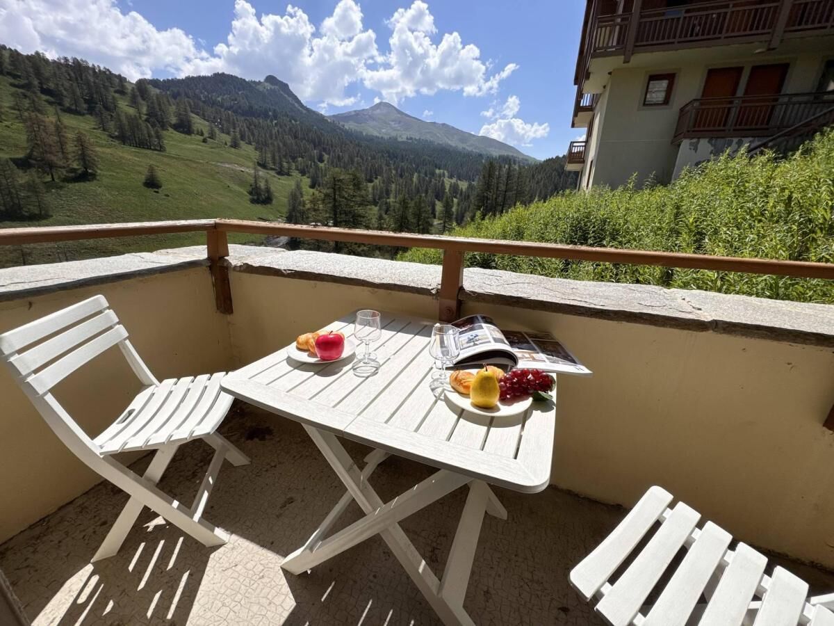 A balcony with a table set for two, a book, and a plate with fruit and a glass.