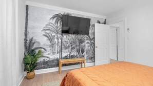 Una camera da letto con un letto, una panca in legno, una TV a muro e una porta.