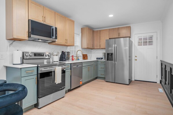 A modern kitchen with stainless steel appliances, light wood cabinets, and a built-in oven.