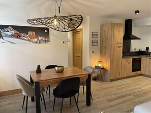 A dining area with a wooden table and chairs, a kitchen with wooden cabinets, and a pendant light. - 140m from ski lifts, 1st floor, terrace, tv, 62m², Morzine (Morzine)