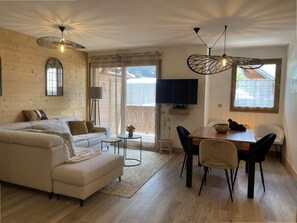 A living room with a sofa, a dining table with chairs, a TV, and a window. - 140m from ski lifts, 1st floor, terrace, tv, 62m², Morzine (Morzine)