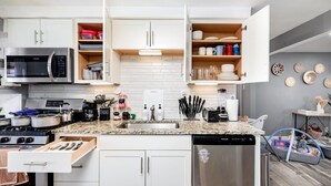 Una cocina moderna con muebles blancos, un microondas de acero inoxidable, lavavajillas y encimera de granito.