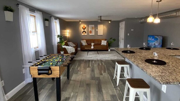 Una cocina moderna con una mesa de futbolín, taburetes de bar y un comedor con sofá.