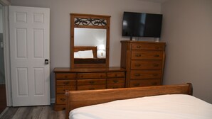 A bedroom with a wooden dresser, a bed, a television on the wall, and a door. - Charming 3-bedroom home with AC in Raleigh (Raleigh)