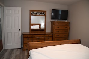 Un dormitorio con un aparador de madera, una cama, un televisor en la pared y una puerta.