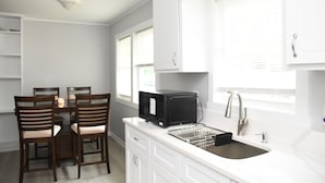 A kitchen with white cabinets, a microwave, a sink, and a dining area with chairs. - Charming 3-bedroom home with AC in Raleigh (Raleigh)