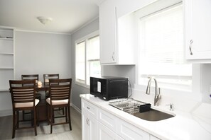 Una cocina con armarios blancos, microondas, fregadero y comedor con sillas.
