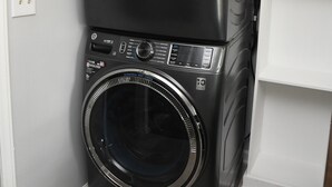 A stacked washer and dryer unit in a corner with a white wall and a wooden floor. - Charming 3-bedroom home with AC in Raleigh (Raleigh)